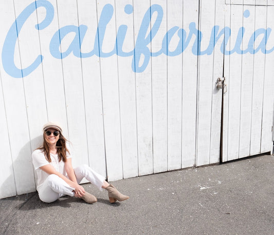 Femme assise sur le sol, adossée au mur, portant un pantalon fluide femme été californie confortable.